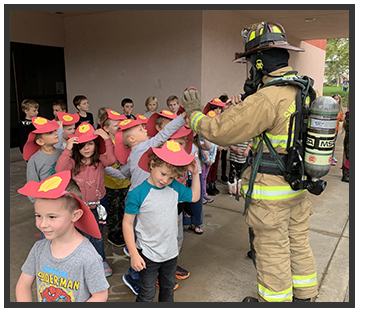 students wearing red and yellow paper fire hats talking to a fireperson