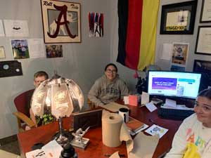 three students sitting at the principal's desk and smiling at the camera