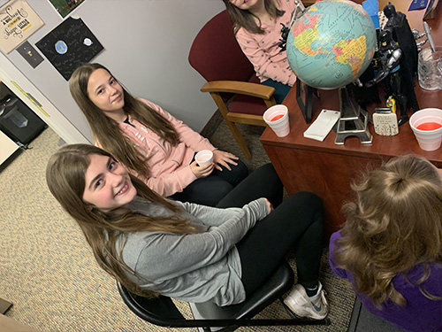 Girls sitting around the principals's desk enjoying refreshments