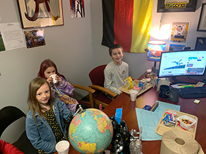 Three students sitting in front of the principal's desk during the Principal's Toast celebration
