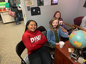 Three girls sitting in front of the principal's desk during the Principal's Toast celebration