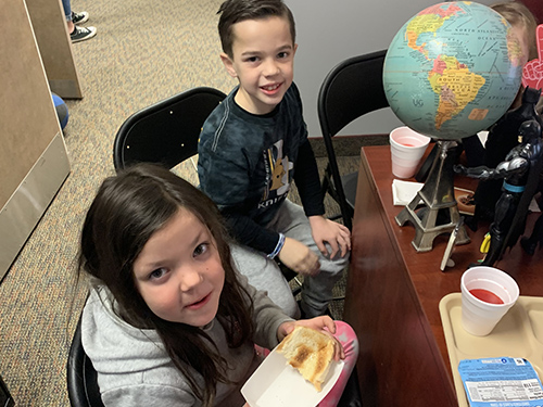 Two students smiling for the camera from the principal's desk