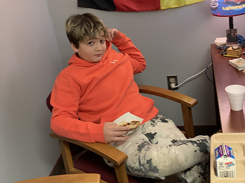 Boy in orange sweatshirt enjoying toast in principal's office