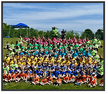 students and staff wearing rainbow colored shirts sitting on lawn