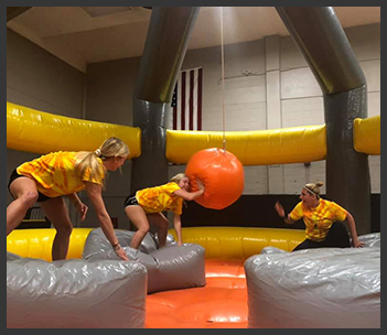 Three students playing in the wrecking ball bounce house arena