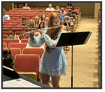 Student in a light blue dress playing a wind instrument for audience