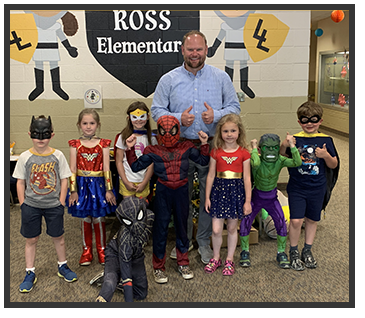 Principal standing next to students in superhero costumes