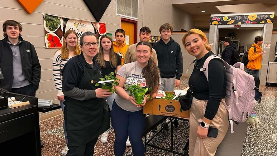 Group of students and staff member in the school hallway holding plants